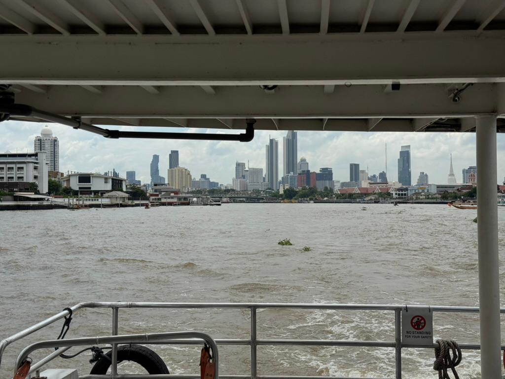 Ferry across the Chao Phraya — Bangkok skyline through overcast morning.